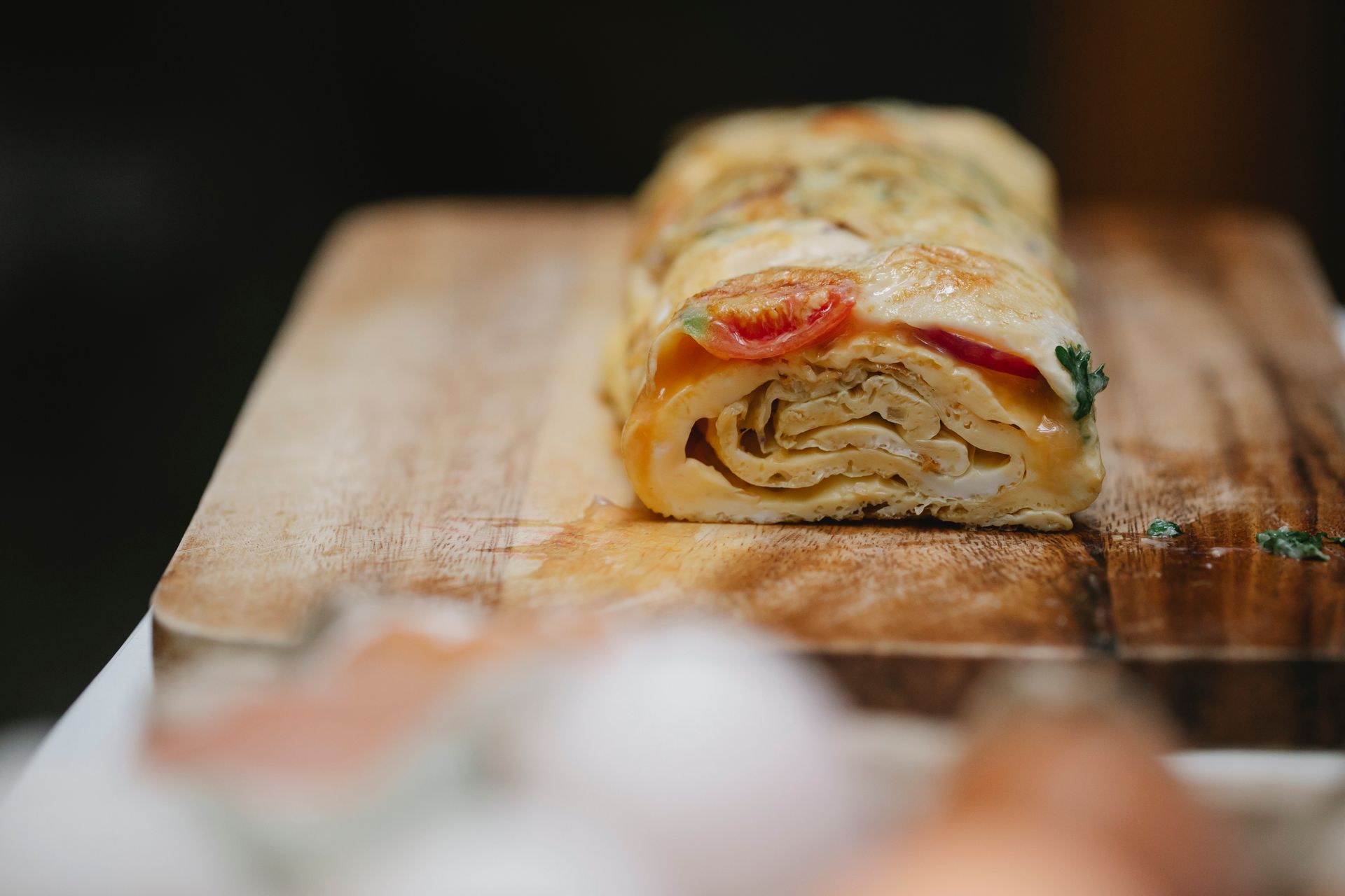 Appetizing yummy egg roll with ripe vegetables and fresh herbs placed on cutting board