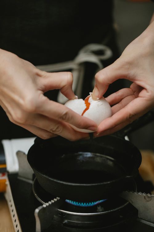 Free Crop anonymous cook breaking raw chicken egg into small frying pan placed on gas stove Stock Photo