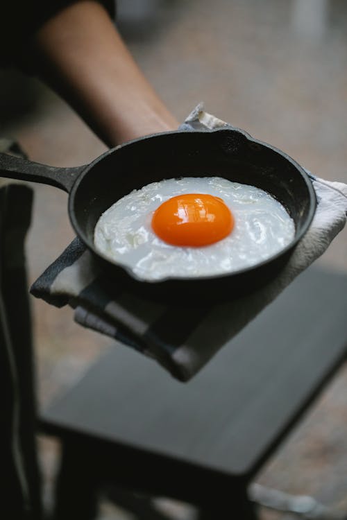 Crop unrecognizable person demonstrating fried egg on pan