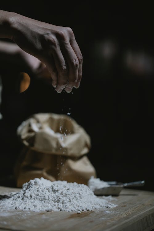 Crop anonymous cook sprinkling flour while standing at table and preparing dough in kitchen