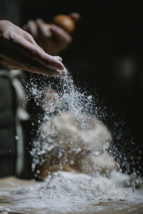 Crop baker scattering powdered flour on table