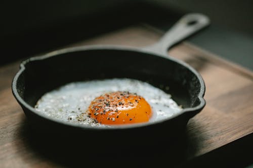 Free High angle of pan with fried egg with seasoning placed on wooden board in kitchen Stock Photo