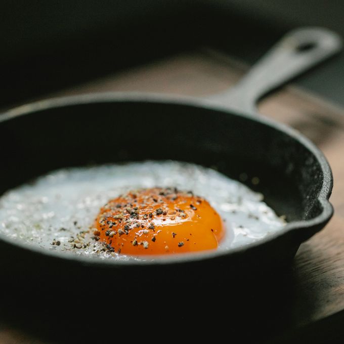 A fried egg cooking in a black skillet on a wooden board — photo by Klaus Nielsen on Pexels