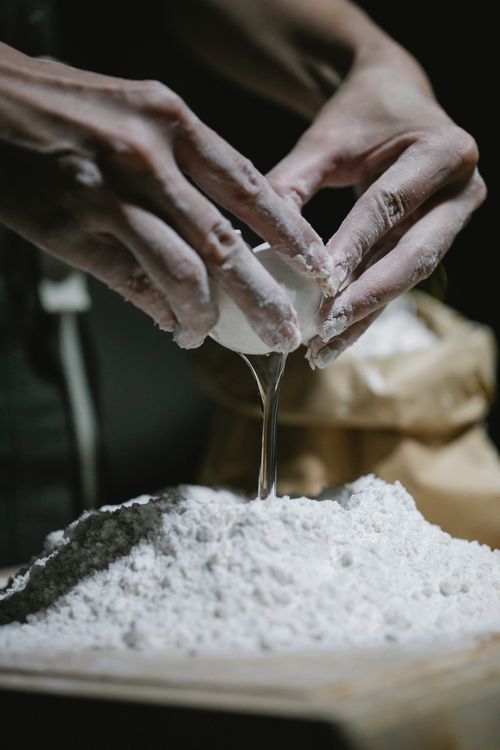 Free Crop anonymous baker breaking egg into dough while preparing ingredients for making dough Stock Photo