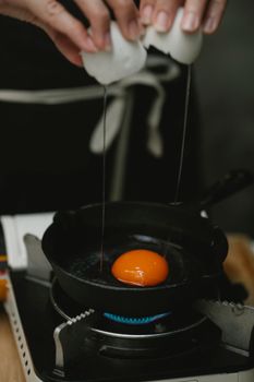 Crop anonymous female in apron cooking fried egg on pan heated on gas stove