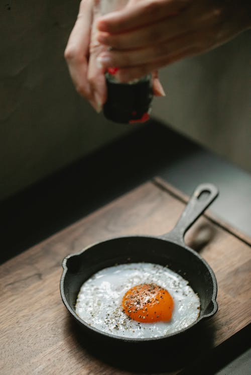 Woman grinding seasoning on fried eggs in pan