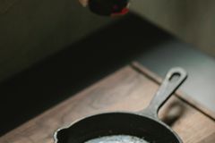 High angle of crop anonymous female adding condiment from mill on fried egg in frying pan placed on wooden board