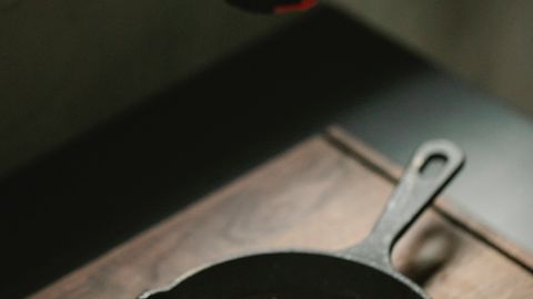 High angle of crop anonymous female adding condiment from mill on fried egg in frying pan placed on wooden board