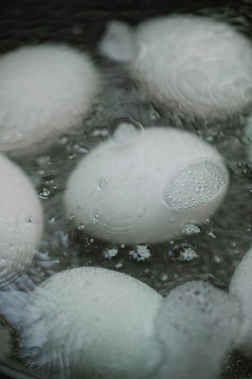 High angle of eggs boiling in hot water with foam in pan in kitchen
