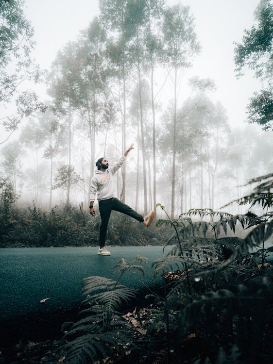 Young man raising arm and leg on road in forest