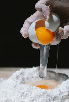 Close-up of hands cracking an egg into flour, perfect for culinary themes.