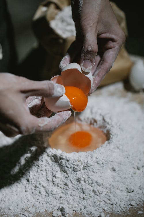 Chef adding egg to flour for dough recipe