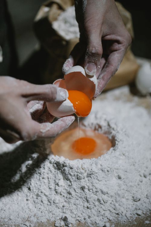 Free From above of crop anonymous baker adding egg to flour while preparing dough for pastry Stock Photo