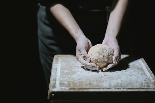 From above of crop anonymous cook kneading dough on wooden board with flour