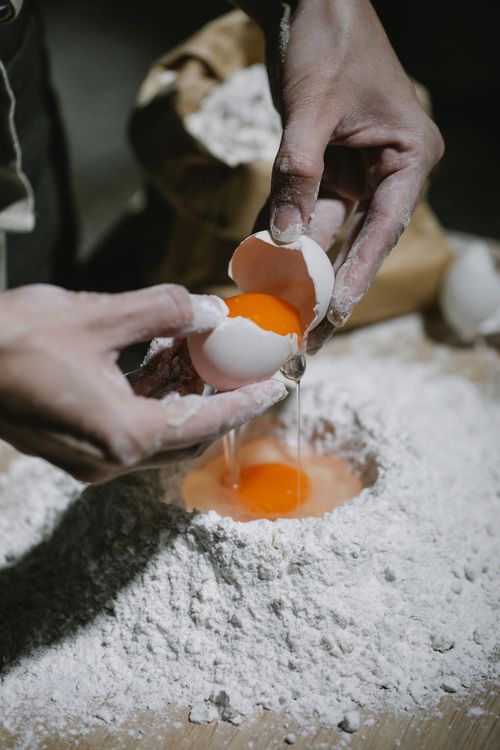 Free High angle of crop anonymous baker adding egg on pile of dough while cooking dough Stock Photo
