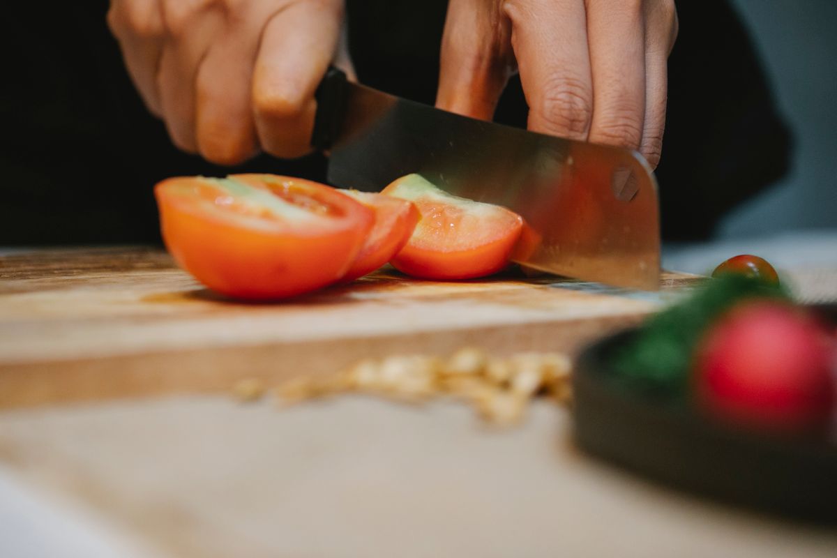 Hands slicing ripe tomatoes on a wooden board — photo by Klaus Nielsen on Pexels