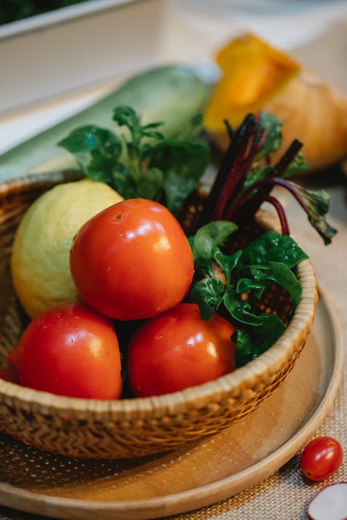 High angle of fresh tomatoes with beet leaves and lemon in wicker bowl and table for cooking process