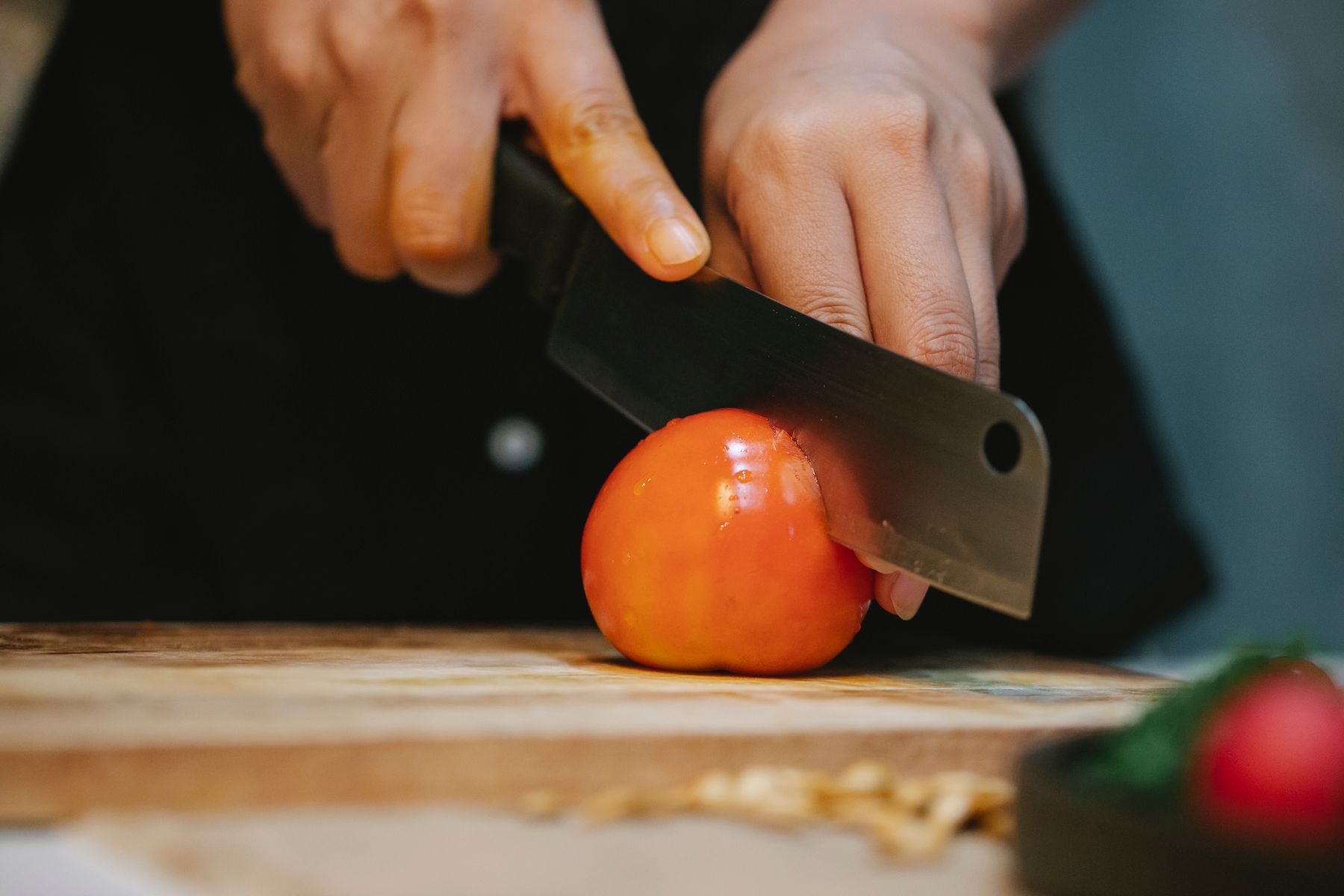 Hands using a kitchen knife to slice a tomato on a cutting board