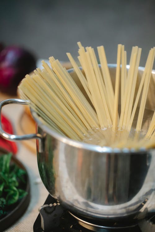 High angle of stainless bowl with spaghetti in hot water cooking on stove in kitchen