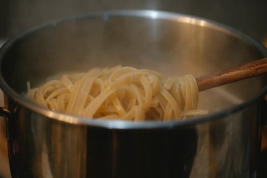 Close-up of steaming spaghetti cooking in a stainless steel pot with wooden utensil.