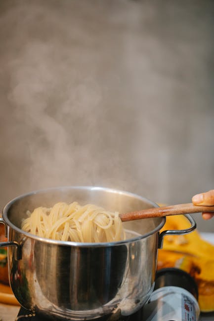 Stainless steel saucepan with boiling pasta water on stovetop`
Image 1 shows a pasta saucepan as the clear, primary subject—a metal pot with pasta and water actively cooking. This directly relates to the article's focus on reheating pasta with cream sauce, as proper cookware is essential to that process.
Image 2 shows pasta already in a skillet/frying pan with sauce, which is a cooking vessel but depicts a later stage and is not the typical "saucepan" used for reheating pasta. The composition also makes the dish itself the primary subject rather than the cookware