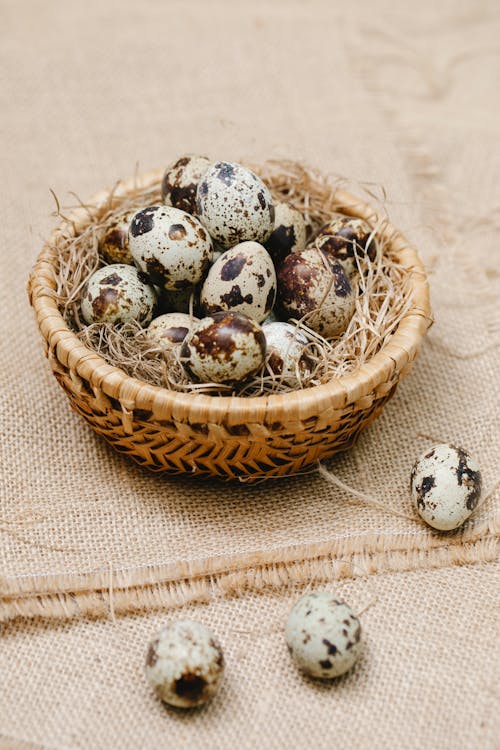 From above of heap of quail eggs on hay in wicker bowl placed on sackcloth