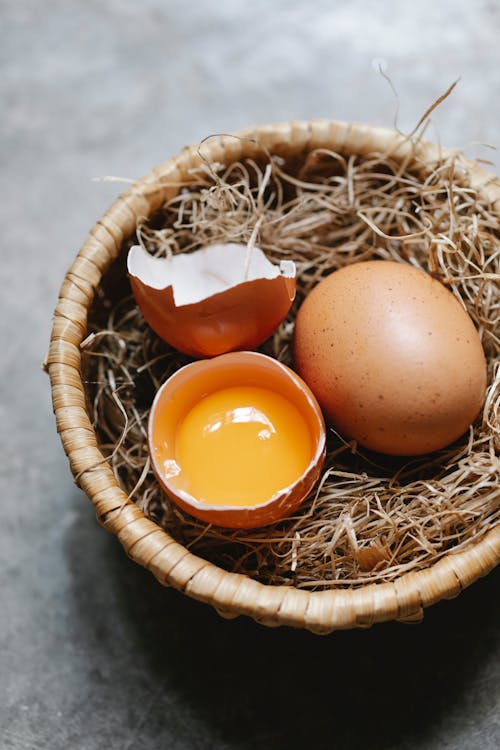 Free Cracked egg placed near whole on hay Stock Photo