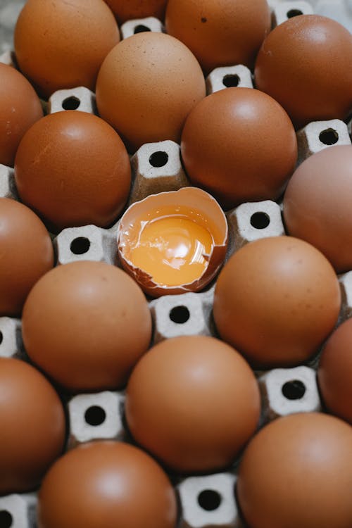 From above of carton container with chicken eggs placed near broken and prepared for cooking