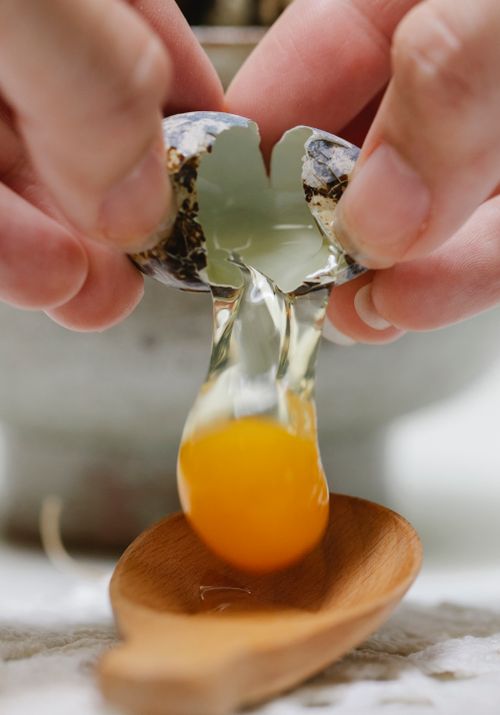 Free Crop unrecognizable person breaking small fresh quail egg in wooden spoon while preparing delicious breakfast Stock Photo