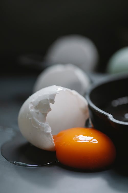 Broken fresh chicken egg placed near row of whole white eggs on black table against blurred background