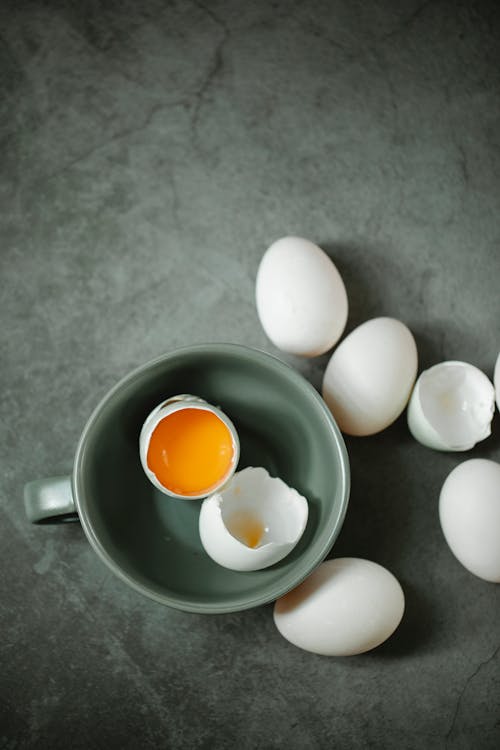 From above of raw chicken eggs placed in ceramic bowl on marble table in daytime