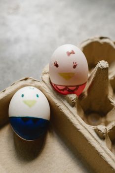 From above of painted Easter chicken eggs with funny faced placed in recycled carton box in daytime