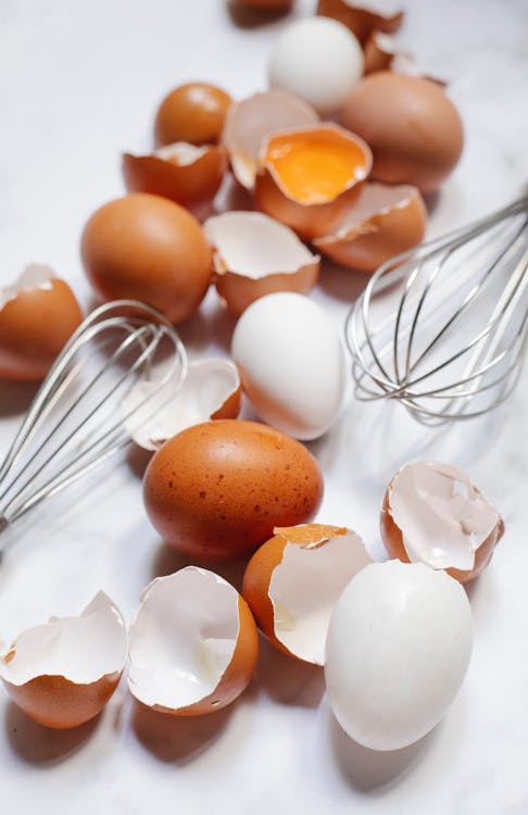 From above of broken chicken eggs and corollas placed on white table in daytime