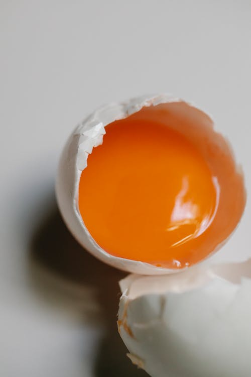 From above of broken white chicken egg with raw yolk placed on light surface