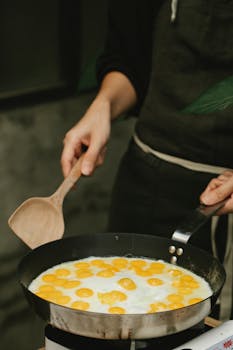 A cook preparing delicious quail eggs in a frying pan in a kitchen setting.