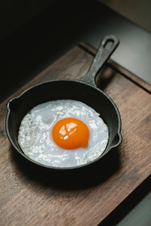 From above of delicious fresh fried egg in metal pan placed on wooden cutting board in daytime