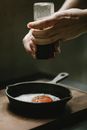 Crop anonymous female chef milling pepper in frying egg in pan placed on wooden board against blurred background