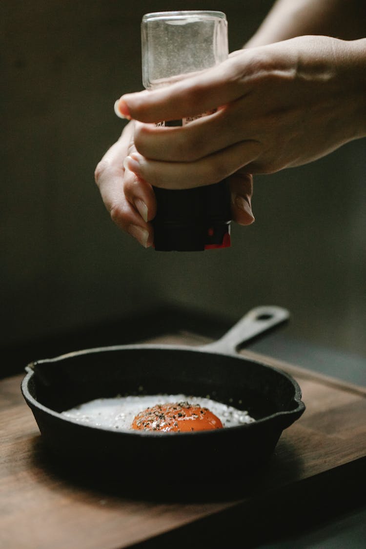 Woman Adding Spices In Frying Egg Placed In Pan