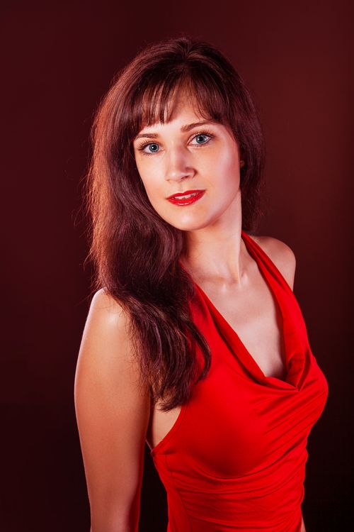 Free Stunning portrait of a young woman in a red dress with a confident pose against a dark backdrop. Stock Photo
