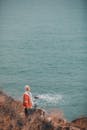 A Man in Red Jacket Standing on the Mountain Near the Ocean