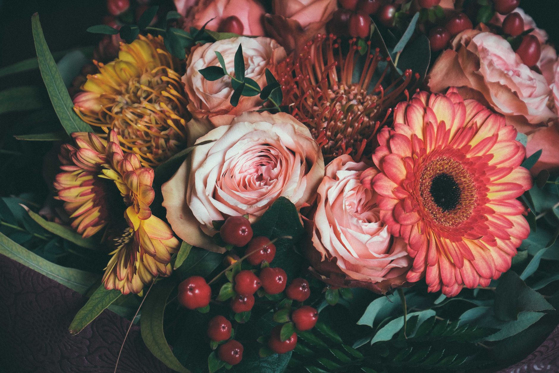 From above of elegant bouquet of fresh pink roses and gerberas arranged with red berried and green leaves