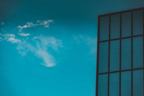 Free Low angle of tall modern building with geometric design and glass walls against bright blue sky Stock Photo
