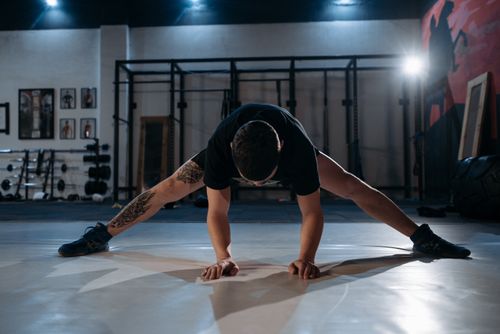 Free A man with a tattoo stretches on a gym floor under dramatic lighting. Stock Photo
