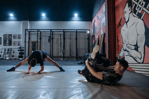Two male boxers stretching and warming up on gym mats before their training session.