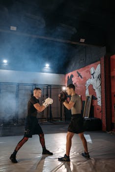 Two men sparring in a smoky gym environment, engaging in combat training.