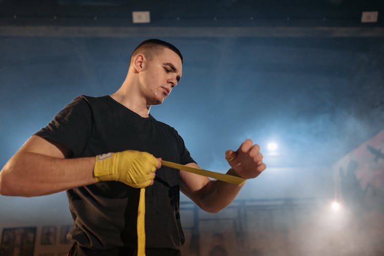 A Man In Black Shirt Putting On His Hand Wraps