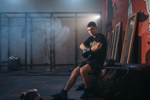 Free A male boxer sitting on a large tire in a gym, wearing gloves and sports attire. Stock Photo