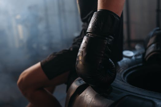 A boxer in black gloves resting their hand on a tire in a gym setting.
