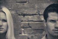 一对夫妇倚靠砖墙摆姿势的艺术特写照，突出了他们的面部表情