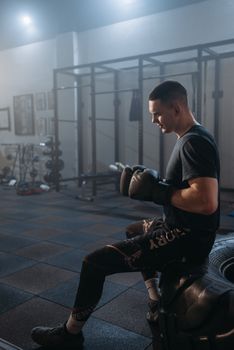A boxer in gloves sits on gym equipment inside a training facility.